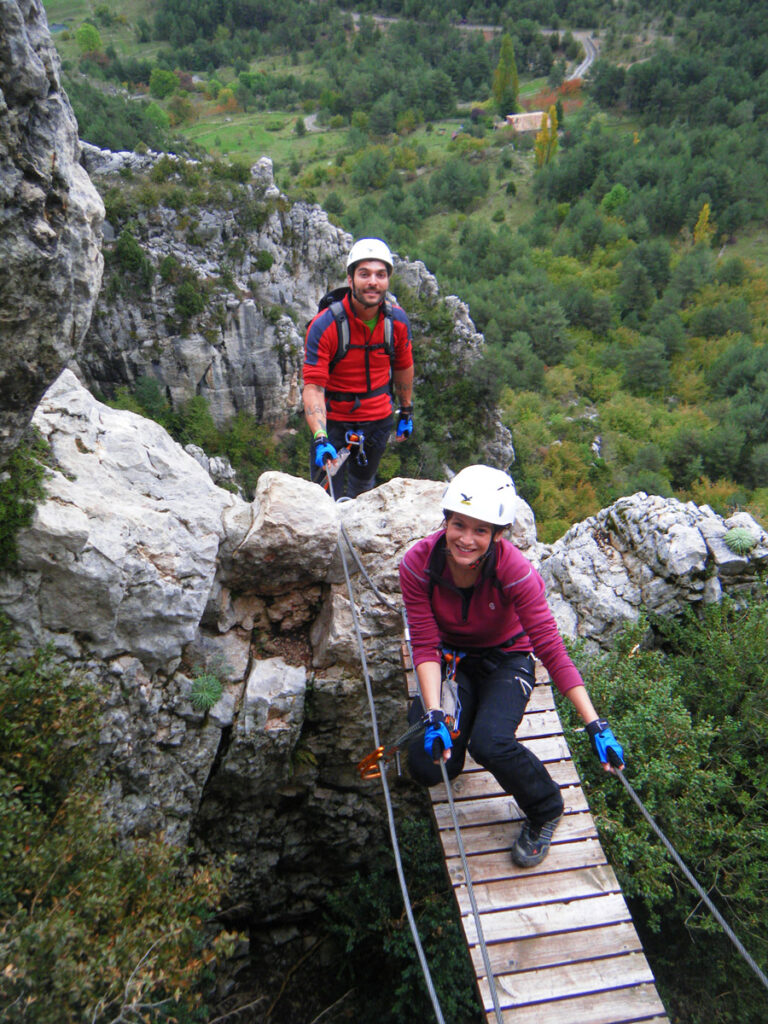 Aventureros cruzando el puente tibetano en la Vía Ferrata de Les Roques de l’Empalomar, con vistas panorámicas de Vallcebre.